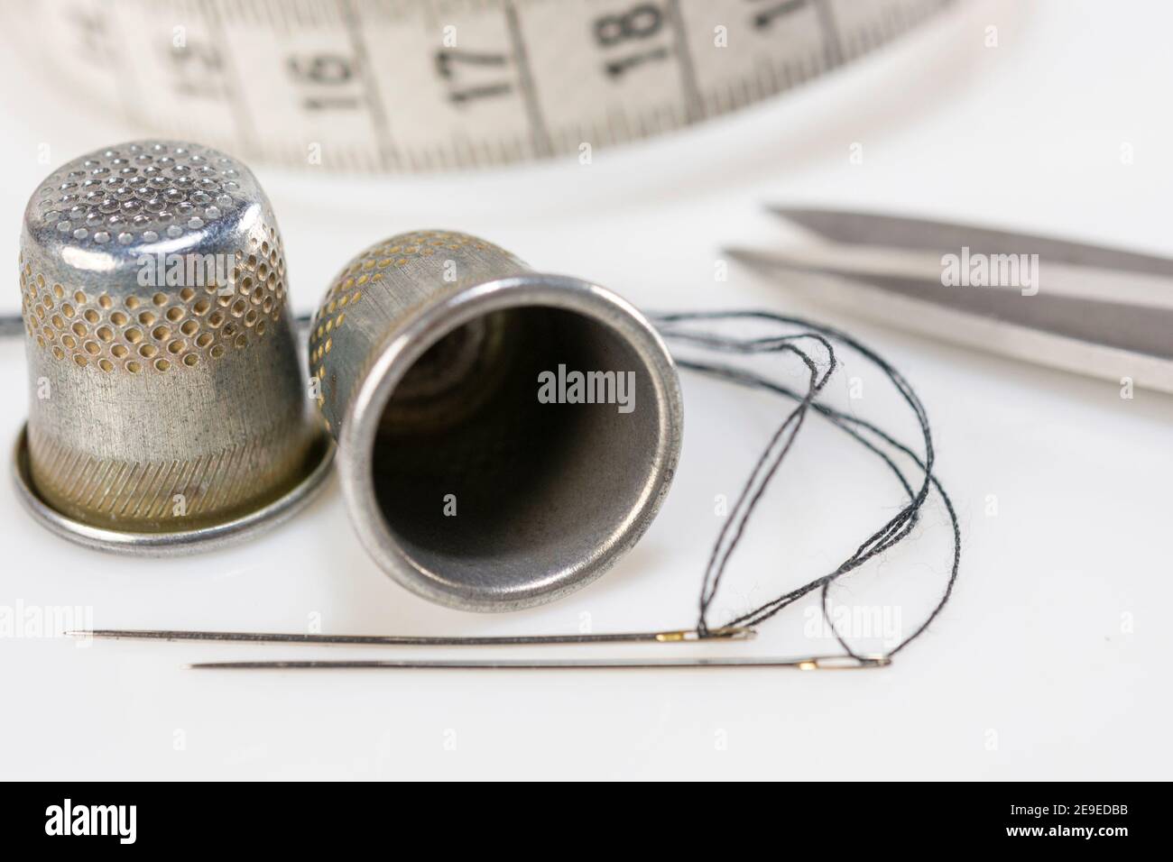 Two sewing thimbles, scissors,  centimeter and two needles with black thread lie on a white background Stock Photo
