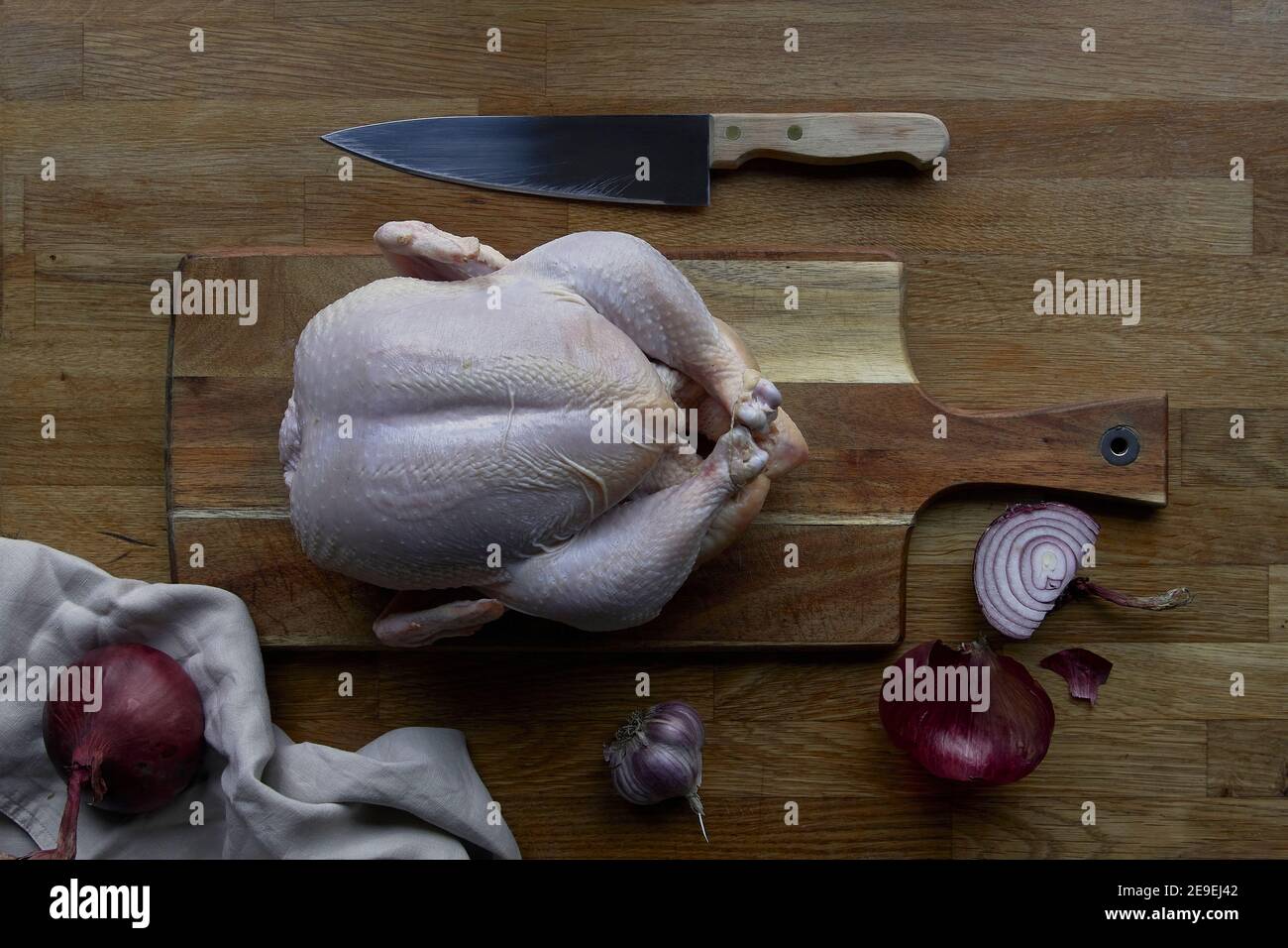 Preparing baked chicken in the kitchen. Wooden worktop, knife and ingredients Stock Photo