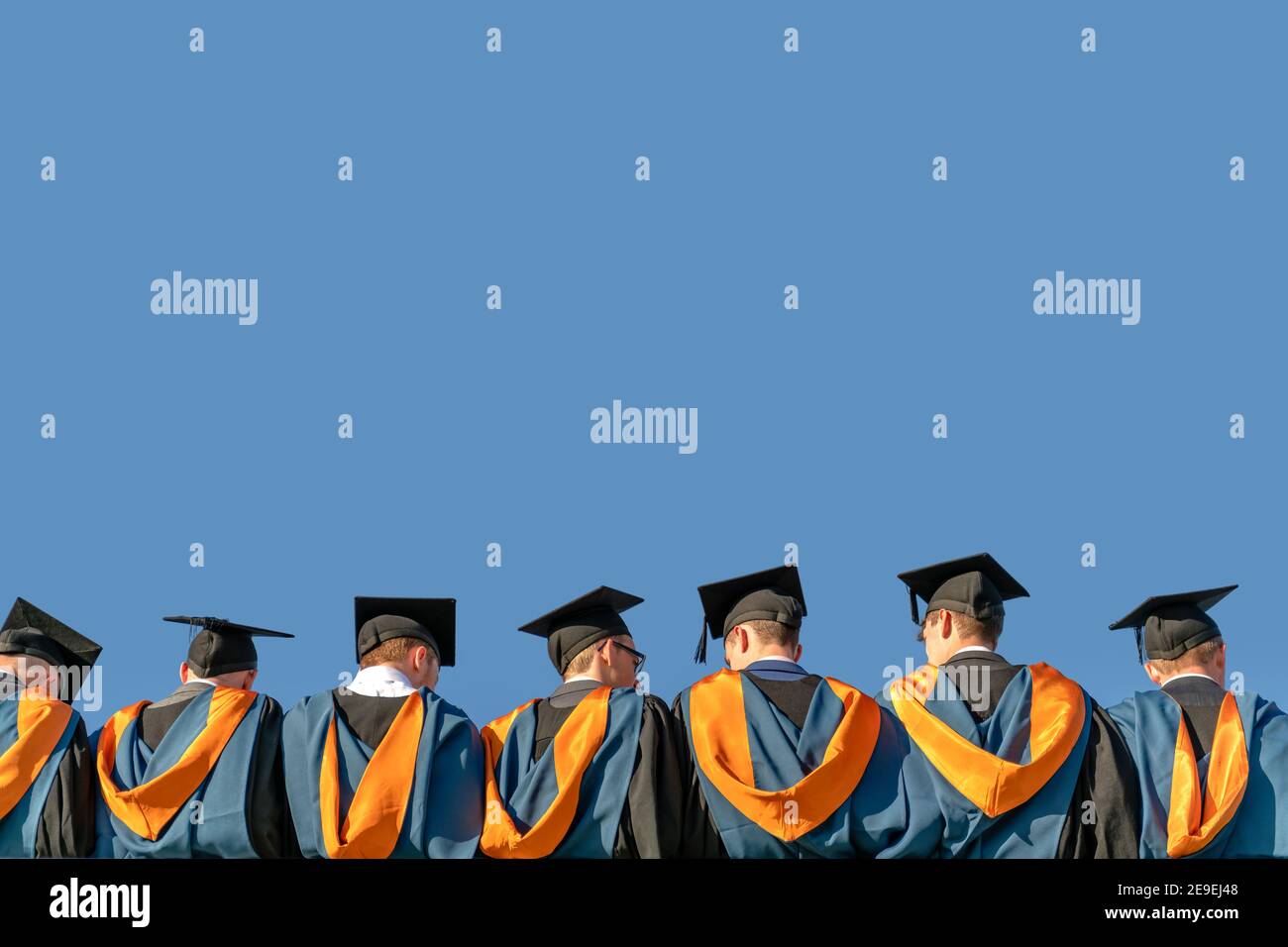 A line of graduates, dressed in gowns and mortar boards, wait in line during their graduation ceremony. Stock Photo