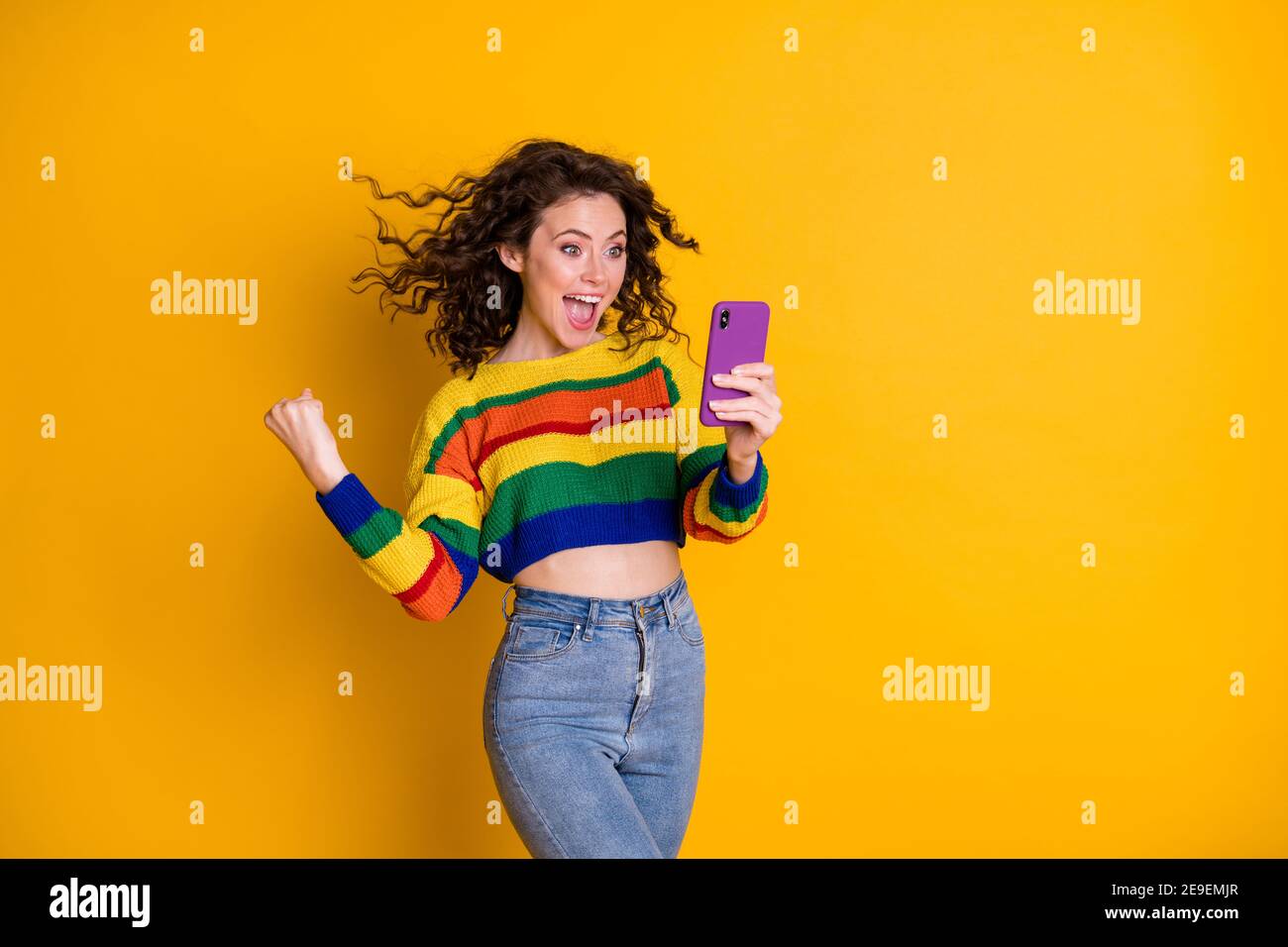 Photo of hooray pretty curly hair girl look telephone wear bright pullover  jeans isolated over shine yellow color background Stock Photo - Alamy