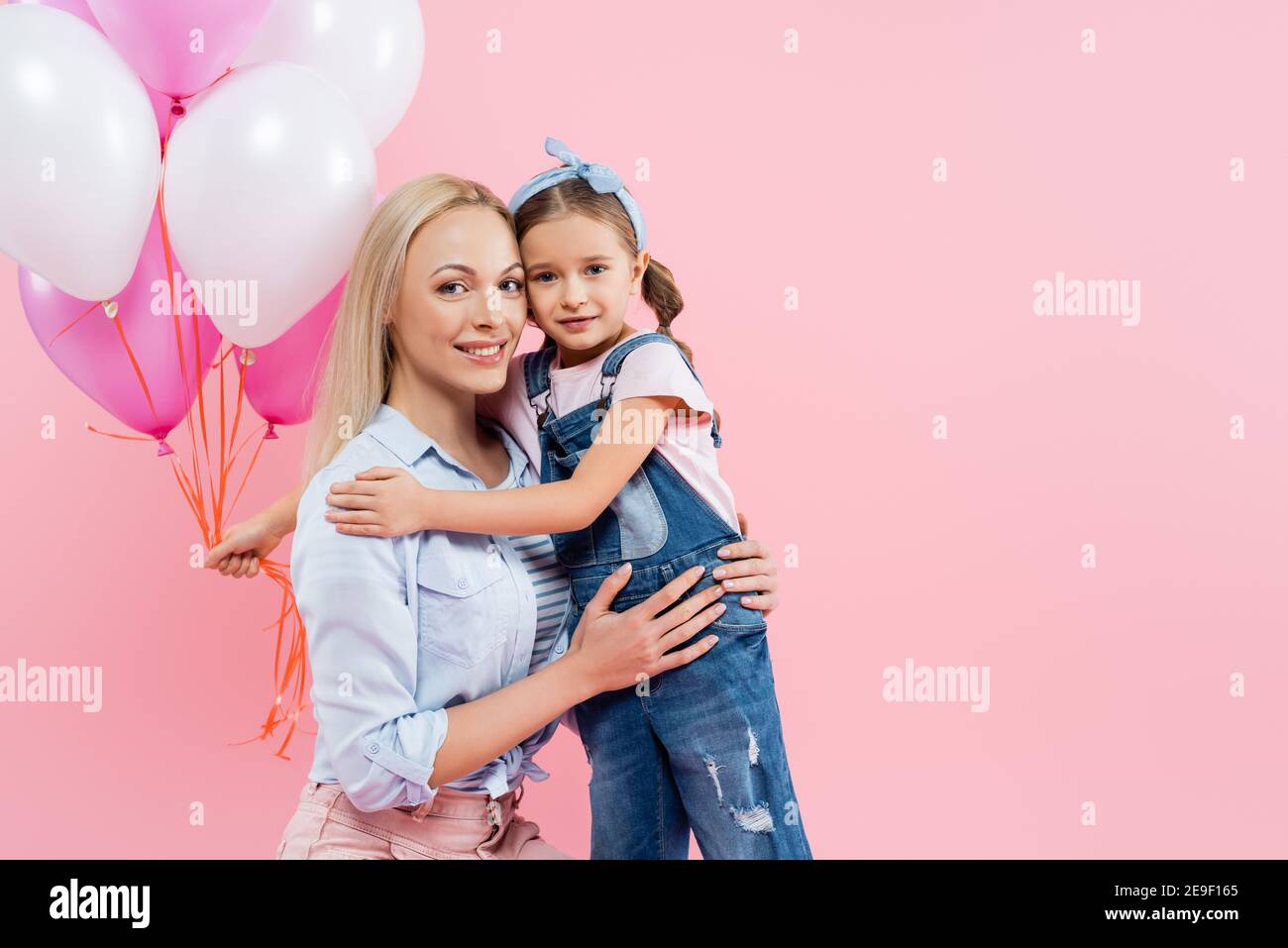 Hugging Balloons happy kid holding balloons and hugging cheerful mother isolated on pink ...