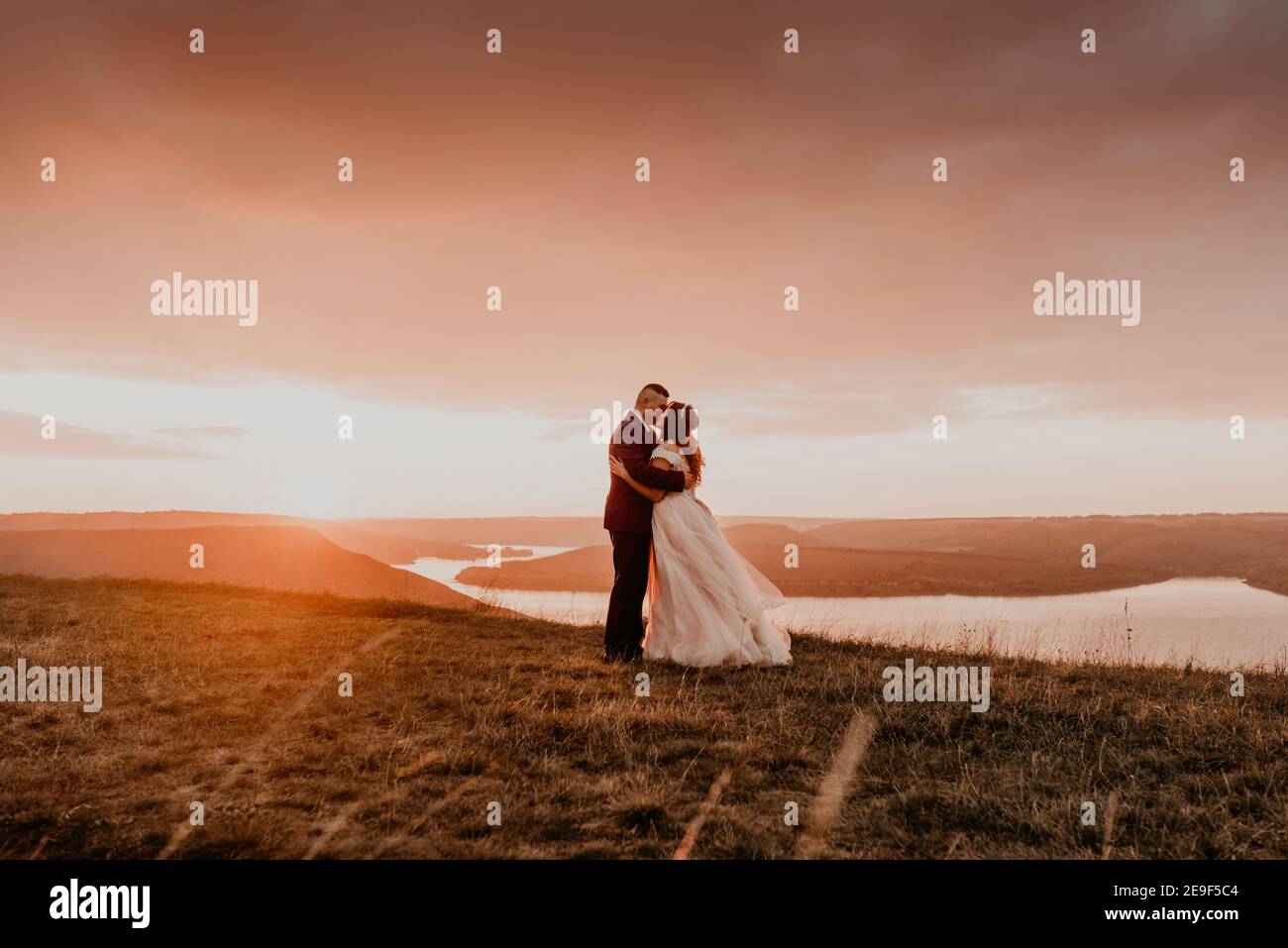 A loving couple wedding newlyweds walk in tsummer in the fall on mountain on cliff above the river. sunset. bride in a white dress with crown on her Stock Photo