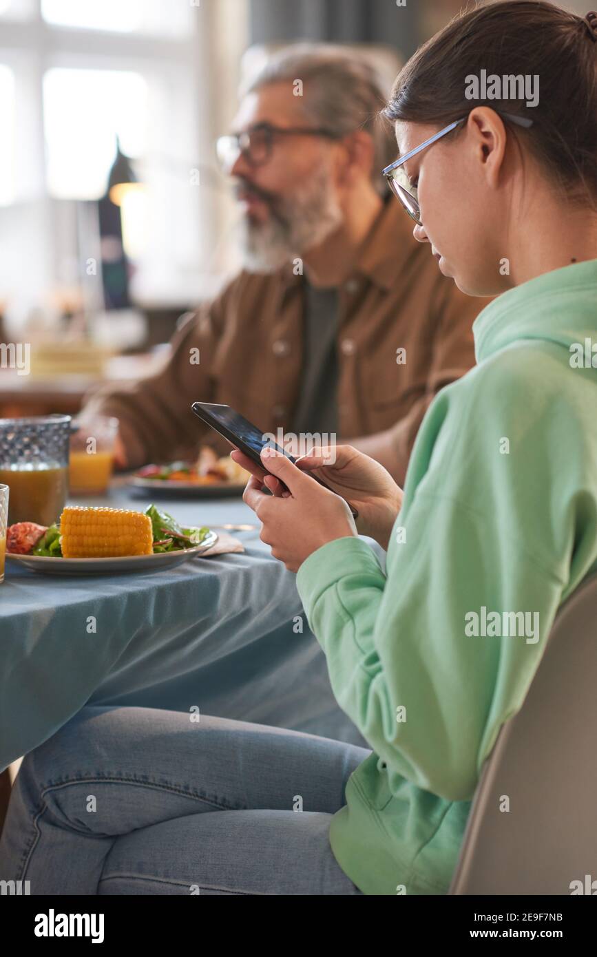Teenage girl using her mobile phone while sitting at the table with her ...