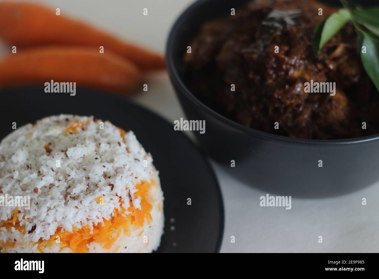 Carrot puttu, a variety of Kerala rice steam cake by adding shredded carrots served along with chicken roast prepared in Kerala style with coconut oil Stock Photo