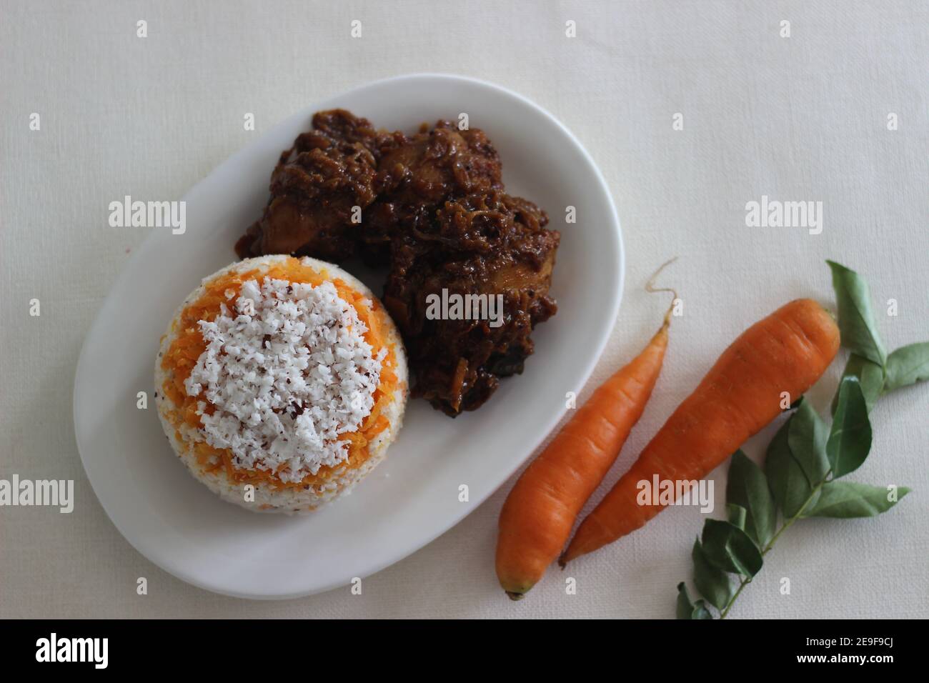Carrot puttu, a variety of Kerala rice steam cake by adding shredded carrots served along with chicken roast prepared in Kerala style with coconut oil Stock Photo