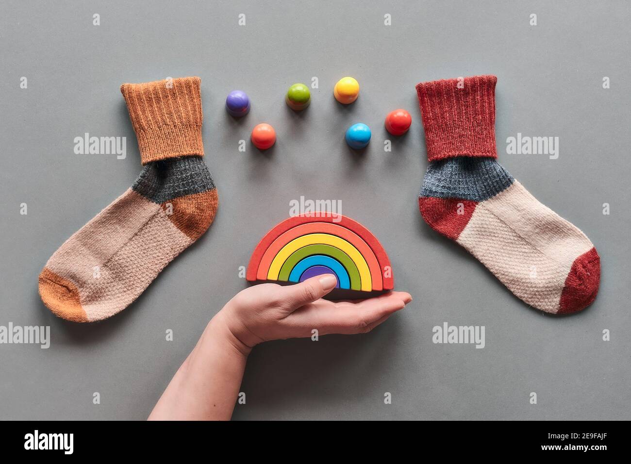 Odd Socks Day. Mismatched socks, hand holding wooden rainbow, toy