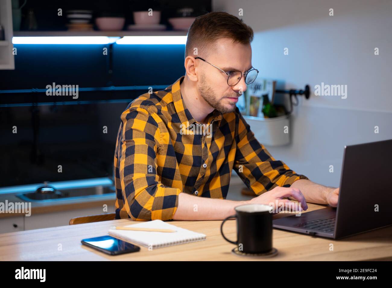 Portrait of male programmer in a yellow-black-gray shirt in a cage and glasses using Programs computer code in a Home. Works professionally on laptop Stock Photo