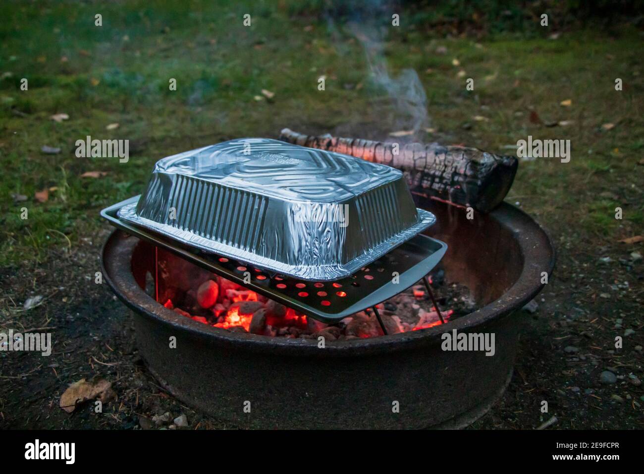 Homemade campfire oven to heat meal with aluminium and perforated pans over bonfire embers Stock Photo