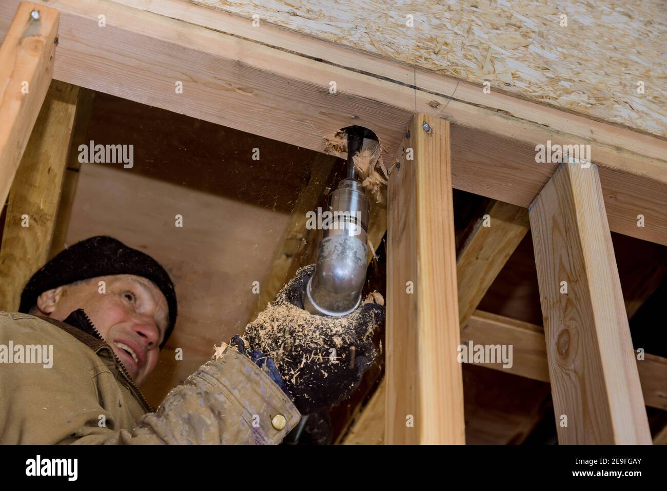 Construction work plumber drilling hole in joist for sewage pipeline