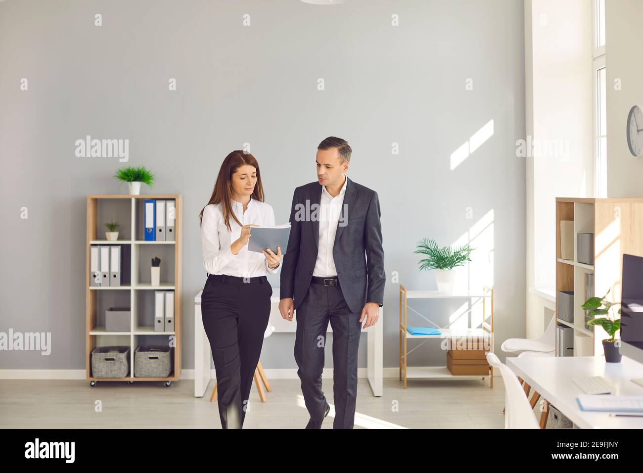 Female office worker shows important documents to her director who is in a hurry somewhere. Stock Photo