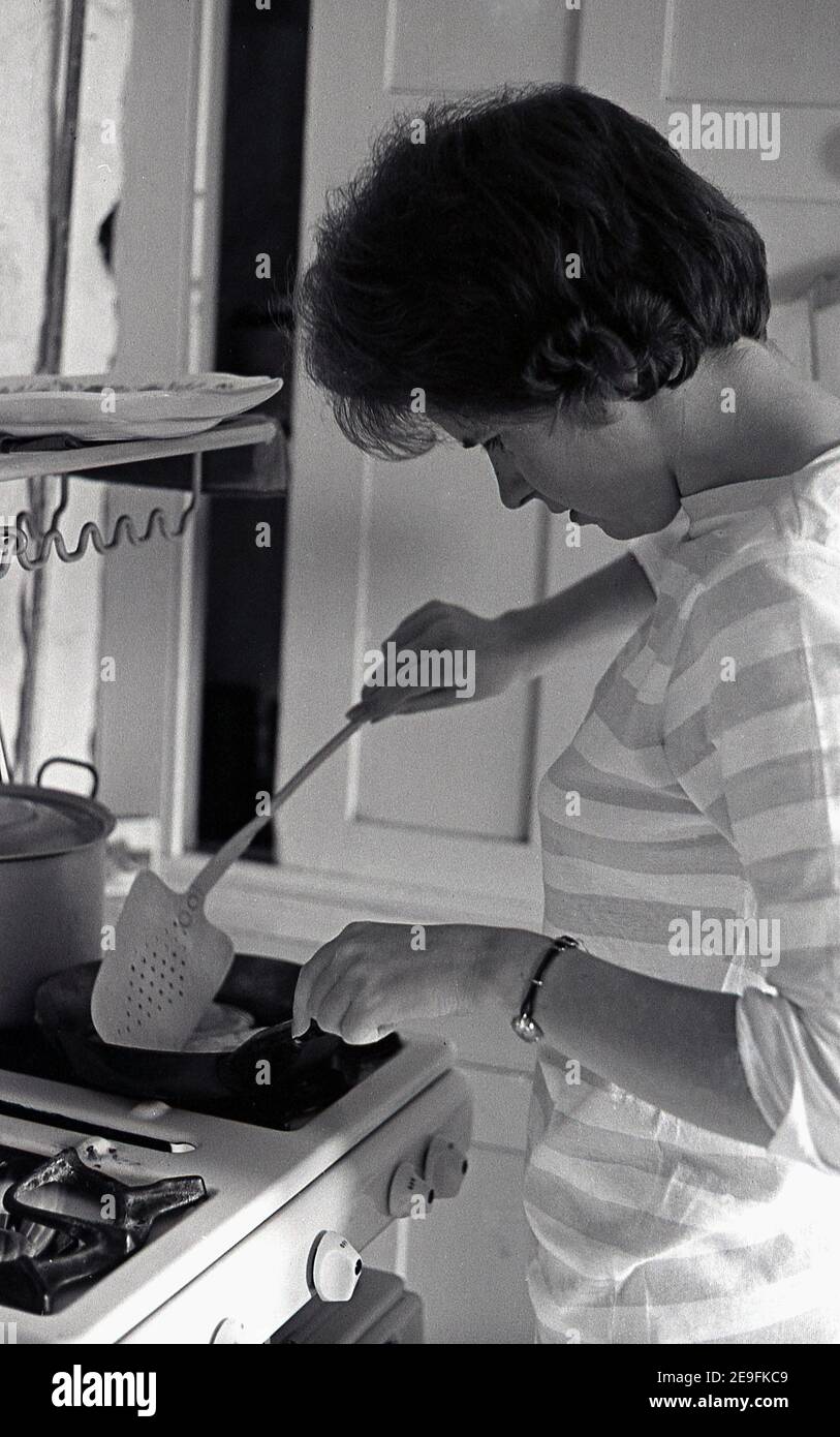 1960s, historical, lad in a small kitchen at a stove with a rying pan ...