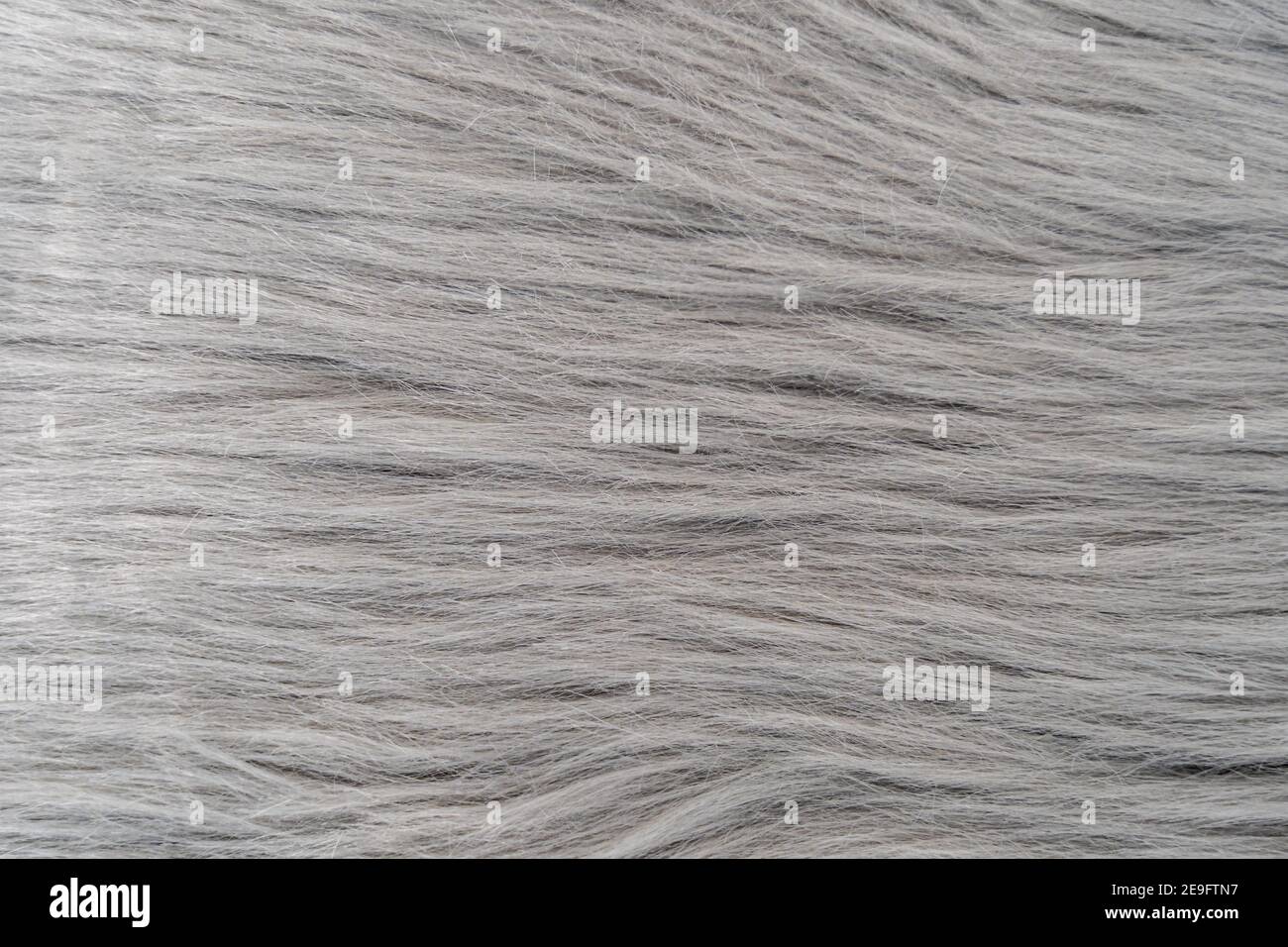 Grey fur rug texture of a textile with long fibers. Natural structure of a soft fabric decoration surface. Fluffy detail looking like animal hair Stock Photo