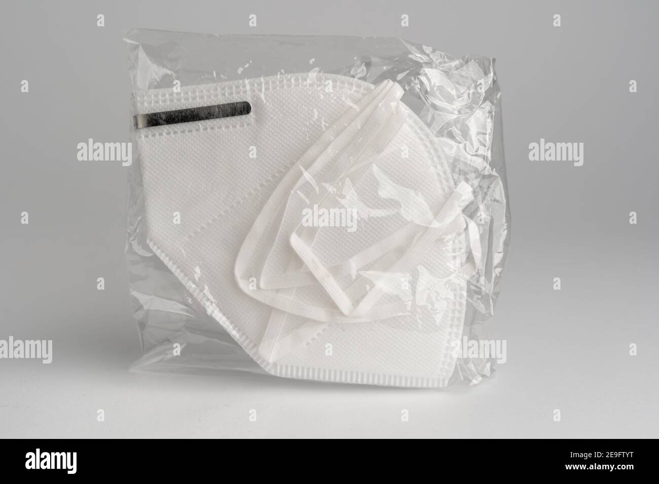 Wrapped FFP2 face mask in white in front of clean background. Certified disposable protection to reduce aerosol emission during Covid-19 pandemic. Stock Photo
