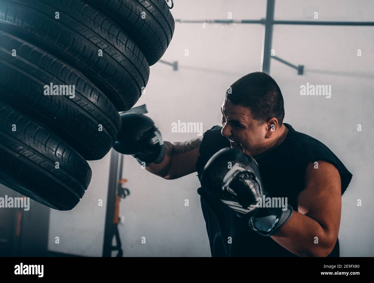 Adult boxer in boxing gloves training with boxing punching tires in a