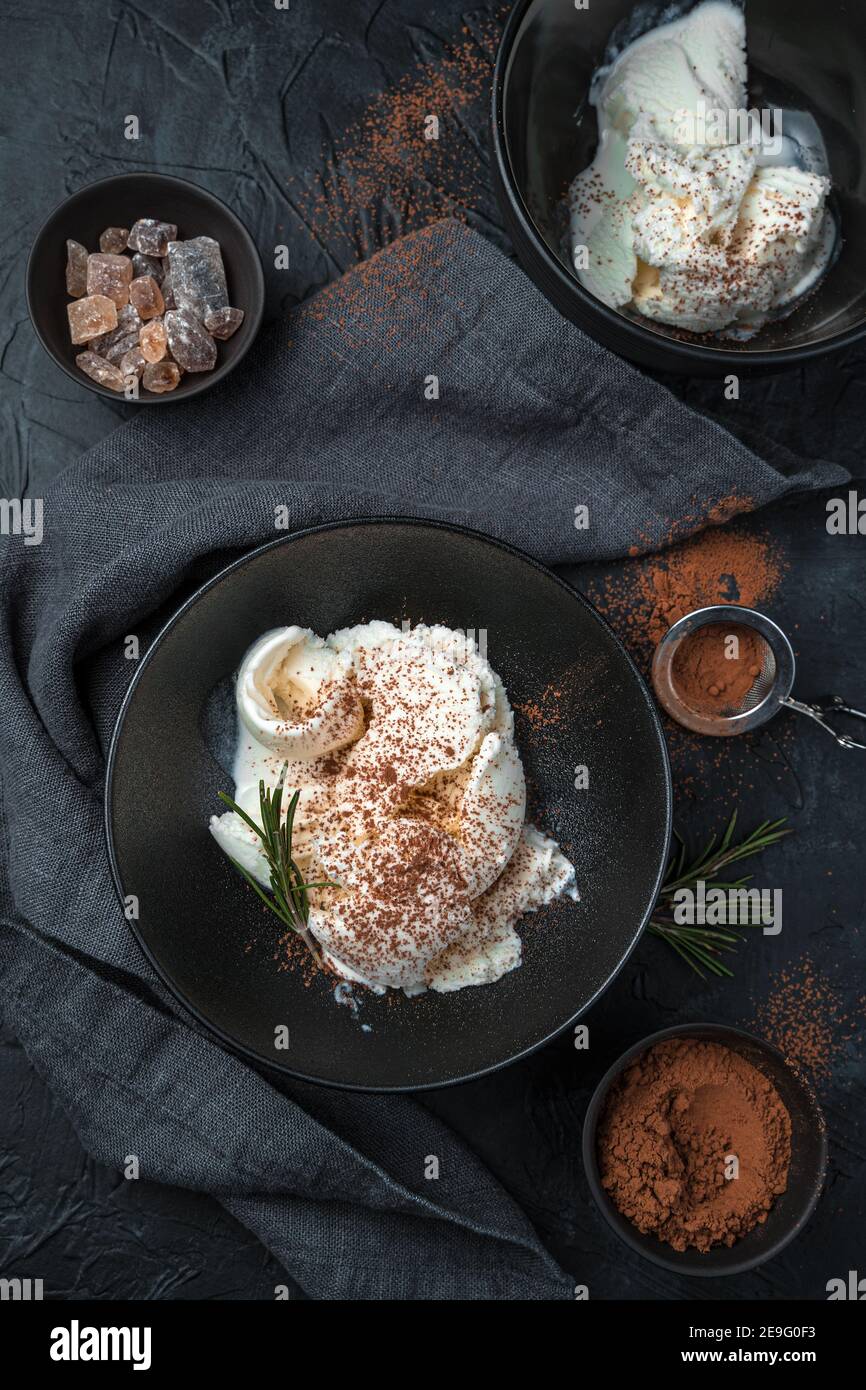 Two servings of cream ice cream and rosemary on a dark concrete