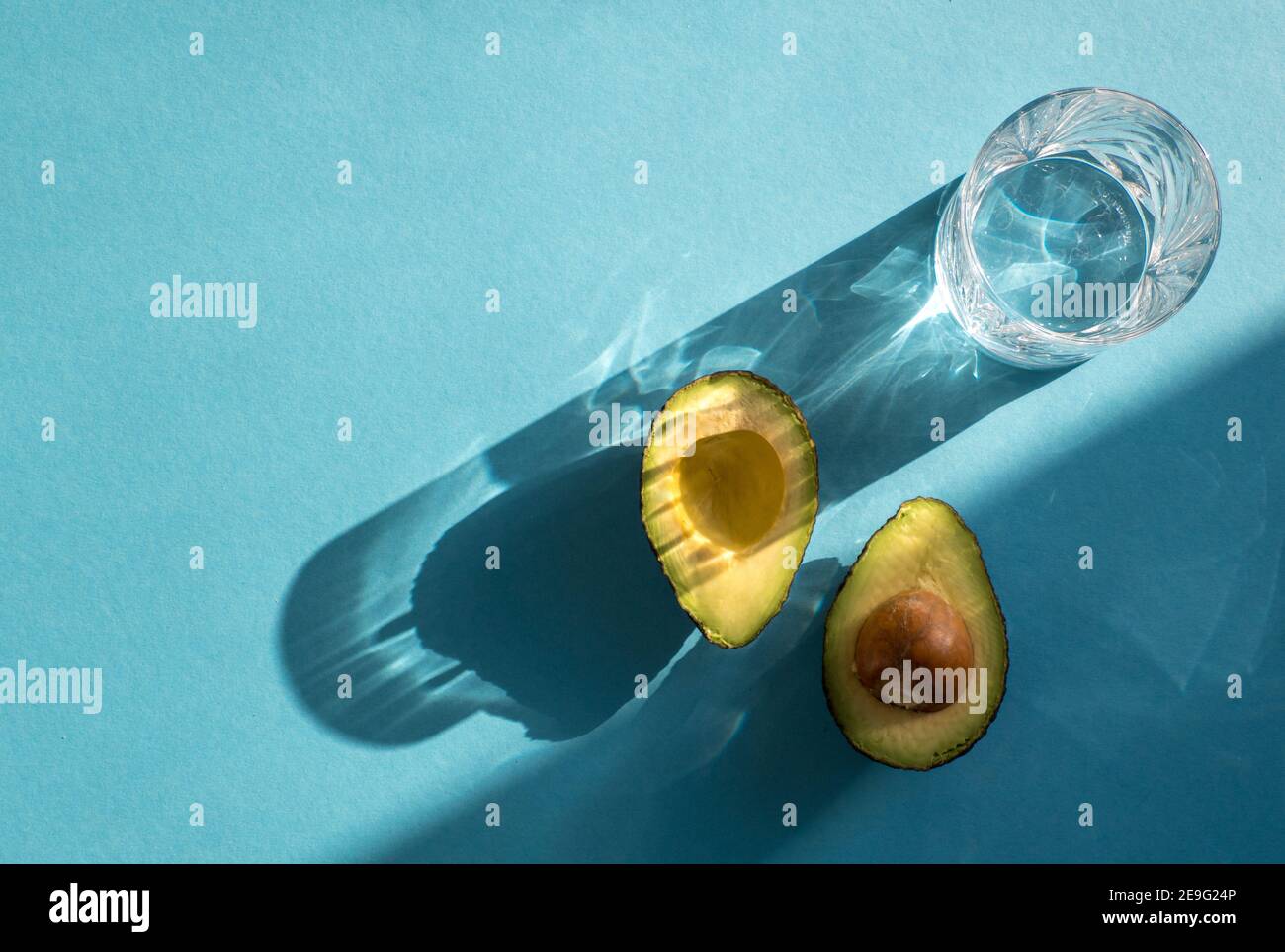 Halved Avocado and a glass of water isolated on blue coloured background Stock Photo