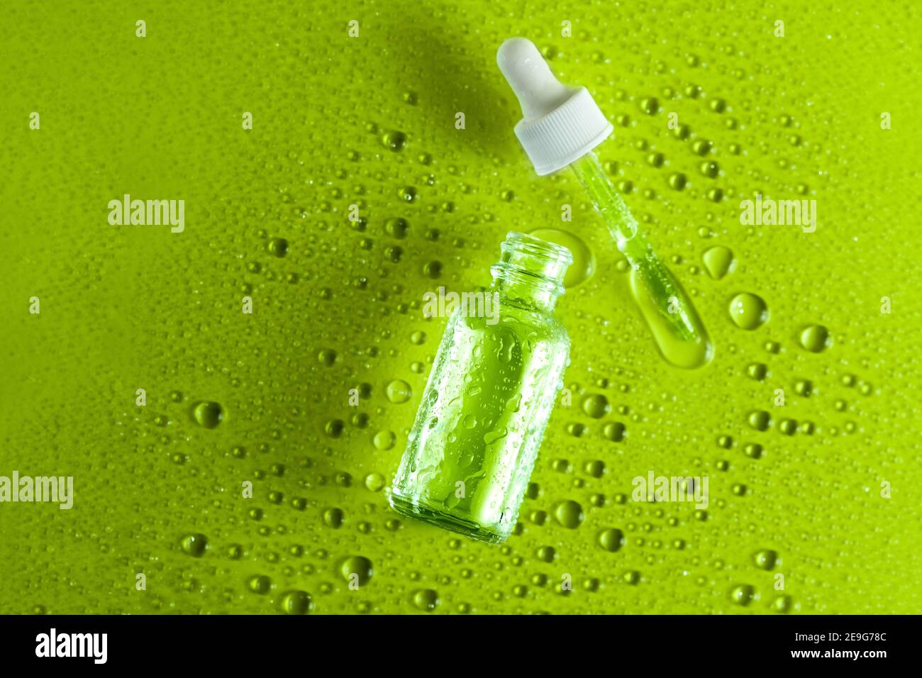 cannabis oil face serum,  alternative medicine and beauty industry. Clear glass bottle with medicine dropper on green background with liquid drops and Stock Photo