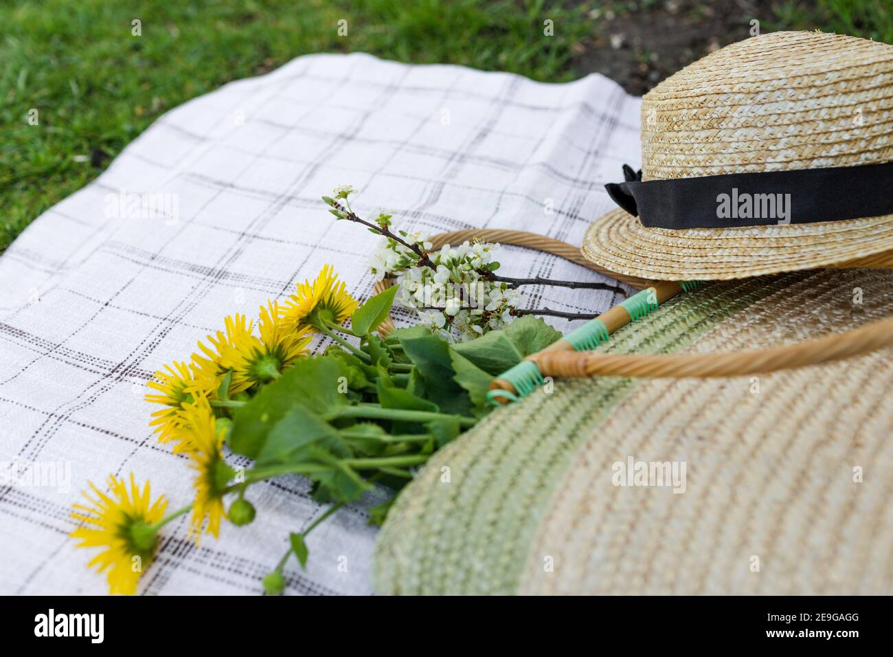 A bouquet of yellow flowers a straw hat and a straw bag lie on the tablecloth. Top view Stock Photo