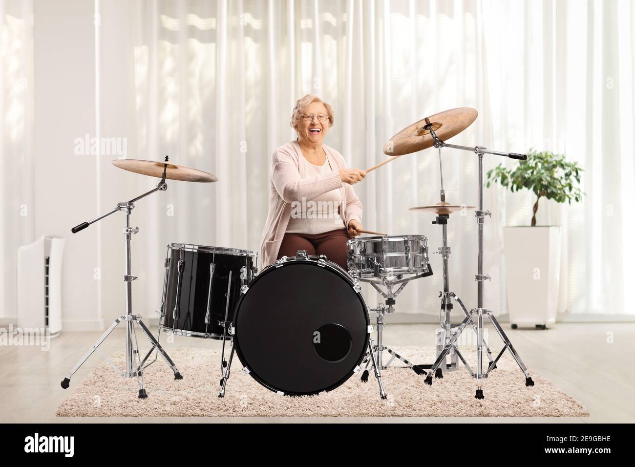 Cheerful elderly woman playing drums at home Stock Photo