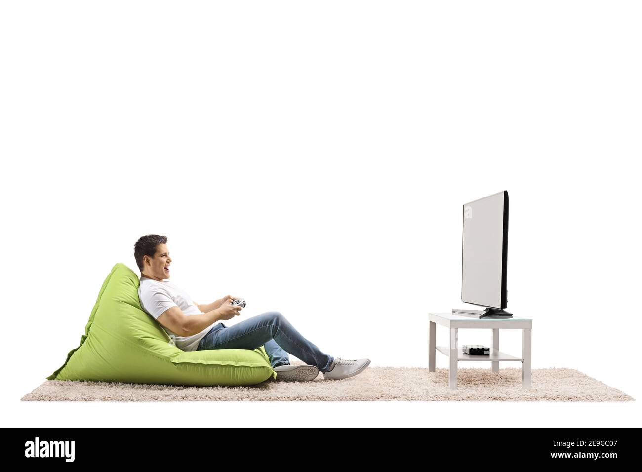 Young man sitting on a green bean bag and playing video games with a joystick at home in a living room Stock Photo
