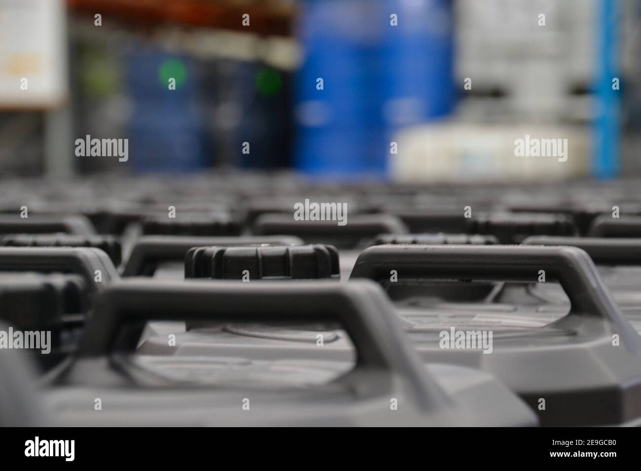 Tops of black plastic chemical containers in a warehouse with blue barrels of dangerous goods in the background Stock Photo