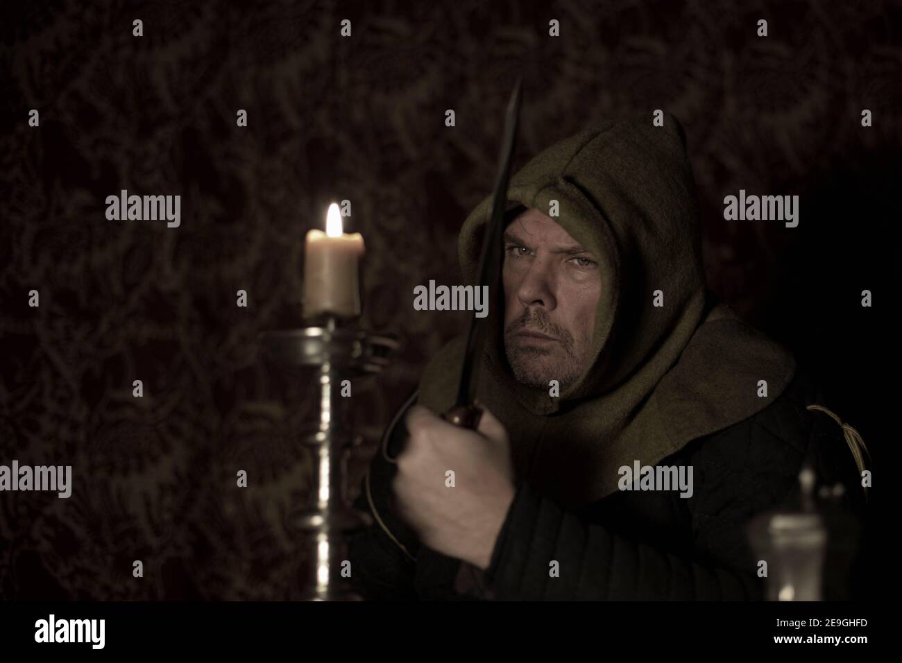 Medieval hooded character sits menacingly by candlelight with dagger Stock Photo