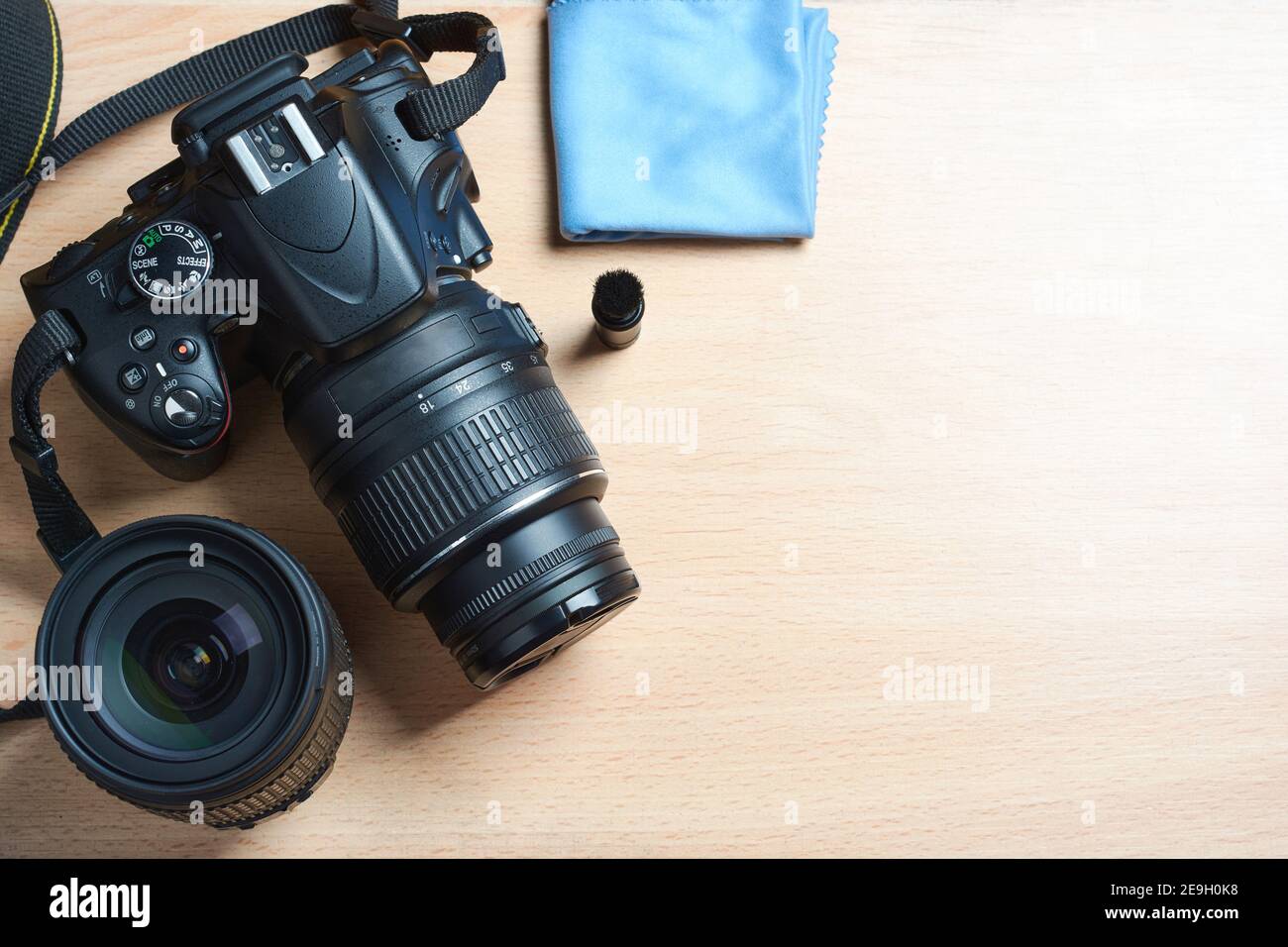 Top view of black digital camera, DSLR with lens, cleaning brush and cloth on wooden desktop with space for text. Stock Photo