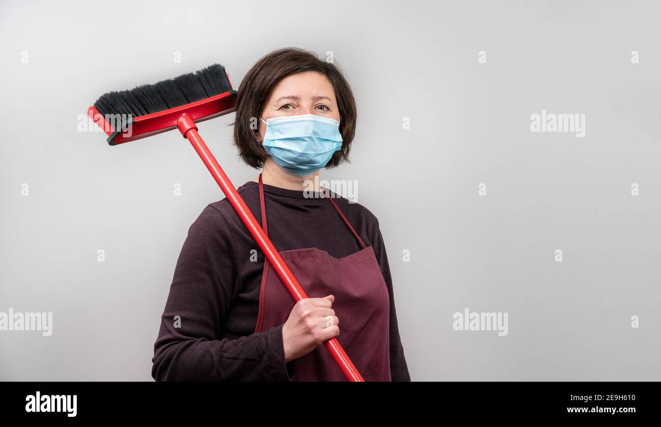Woman holding a broomstick over her shoulder wearing an apron and a mask. Isolation during the Covid pandemic. Stock Photo