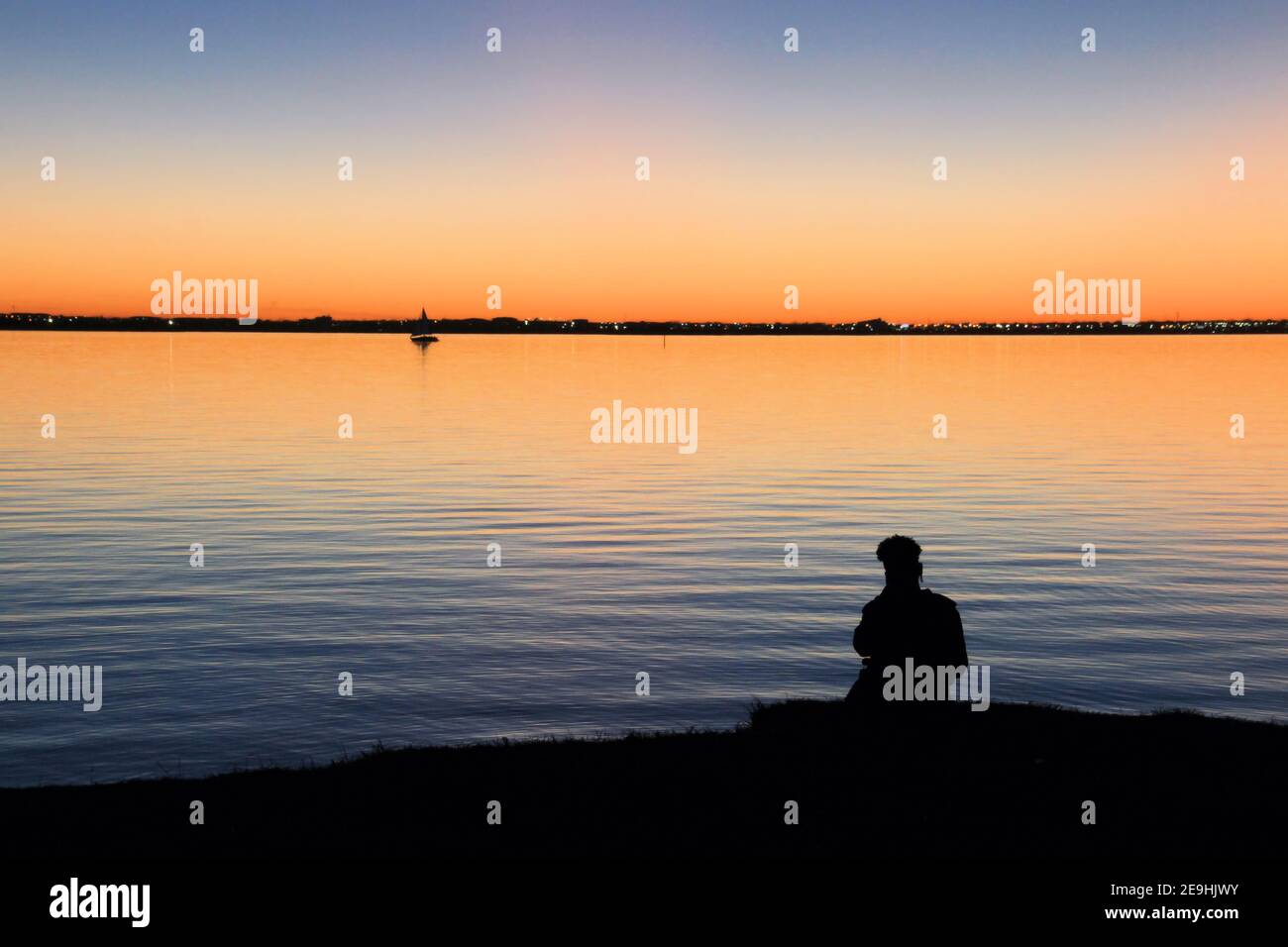 A boy is silhouetted against a beautiful sunset over Lake Hefner in Oklahoma City. Stock Photo