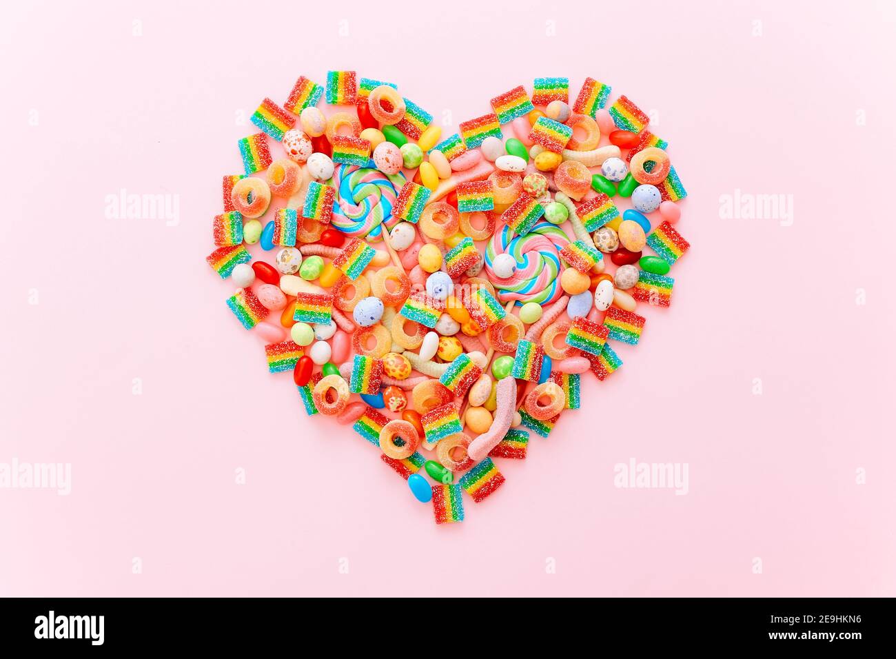 Heart made of colorful sugar candies on a pink background. Valentine's Day concept. Top view, flat lay. Stock Photo