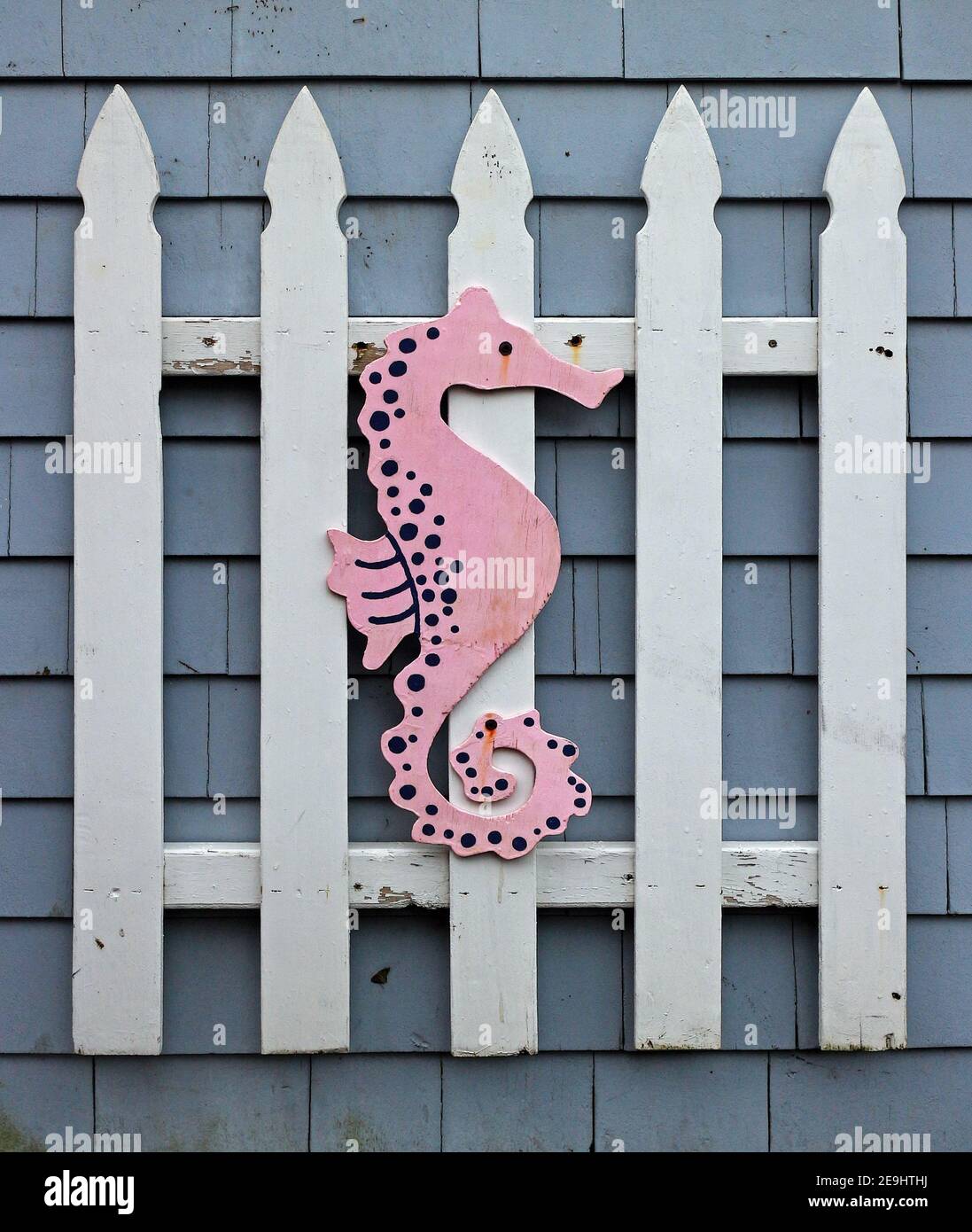 Pink seahorse decoration attached to a white picket fence on the side of a house. Stock Photo