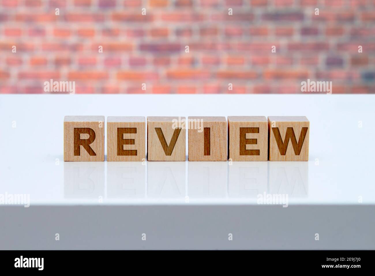 'Review' message sign on wooden blocks sitting on a white table with brink wall on the background. Stock Photo