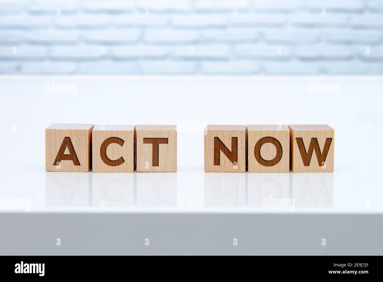 'Act Now' message sign on wooden blocks sitting on a white table with white brinks on the background. Stock Photo