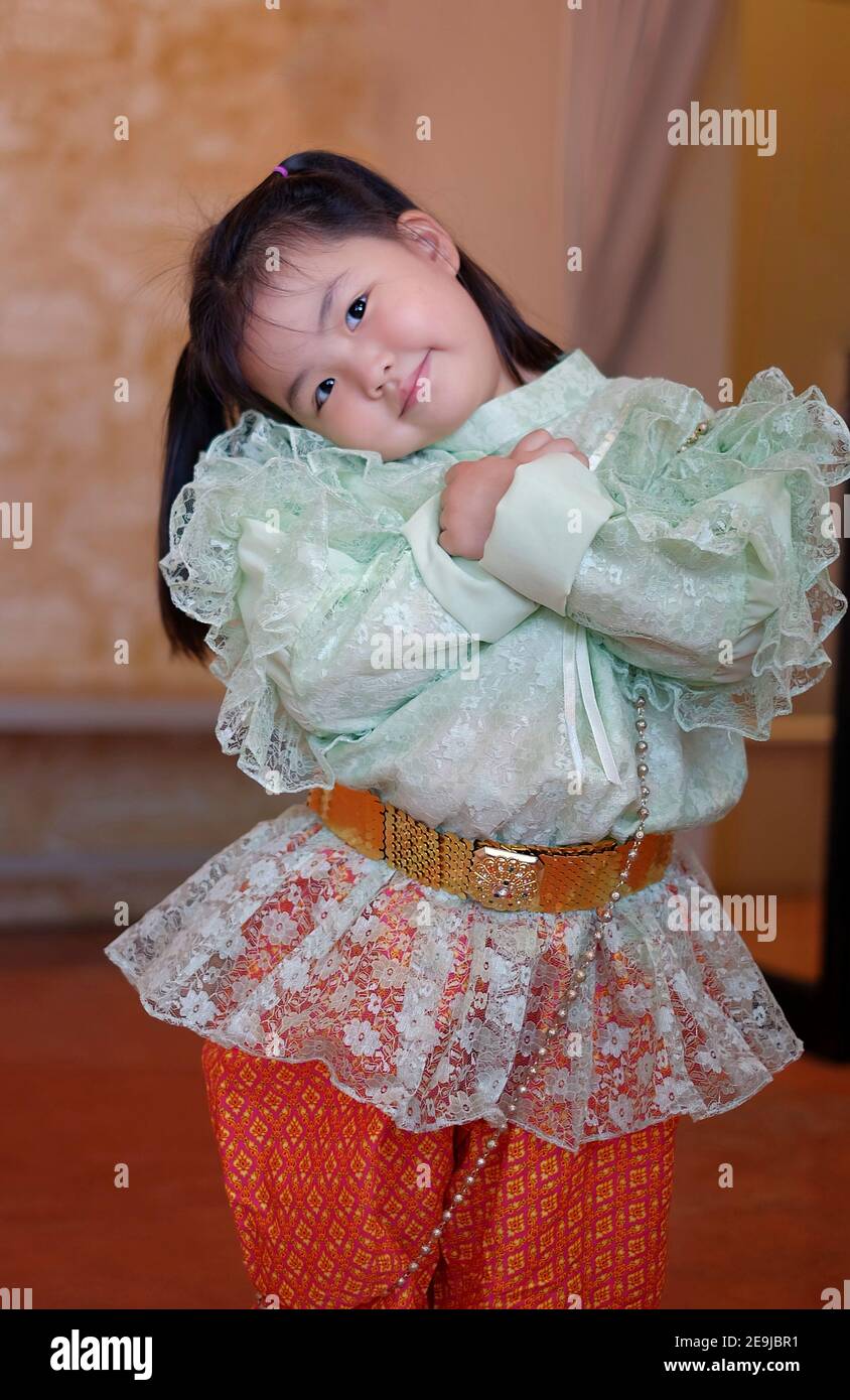 A cute young Asian girl is wearing a traditional green and orange Thai costume during Songkran festival in Thailand. Stock Photo