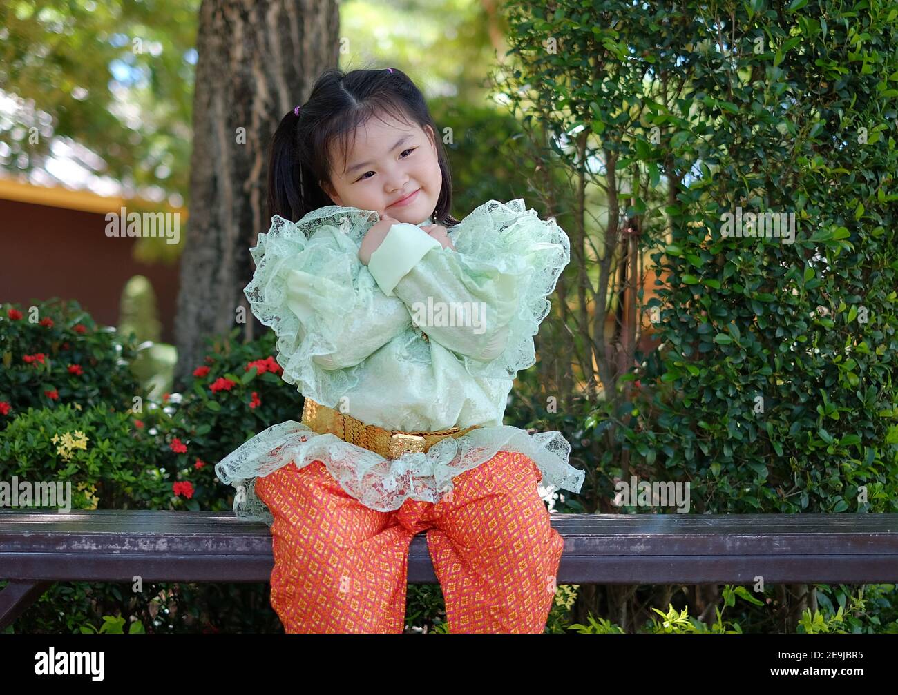 A cute young Asian girl is wearing a traditional green and orange Thai costume during Songkran festival in Thailand. Stock Photo