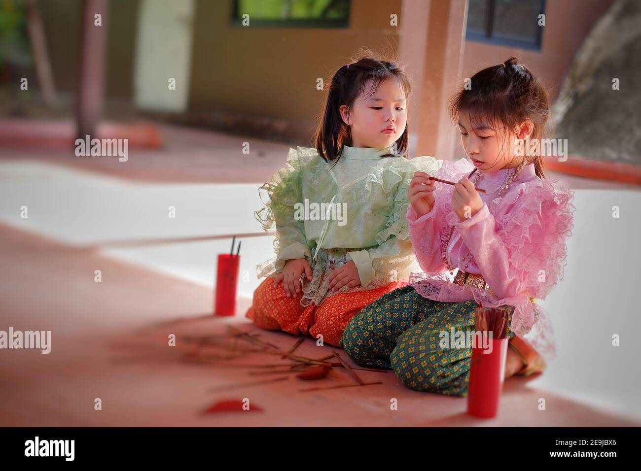 Cute young Asian girls in traditional Thai costumes are shaking chi-chi sticks, also known as Kau chim  or Kau cim sticks during a festive Thai new ye Stock Photo