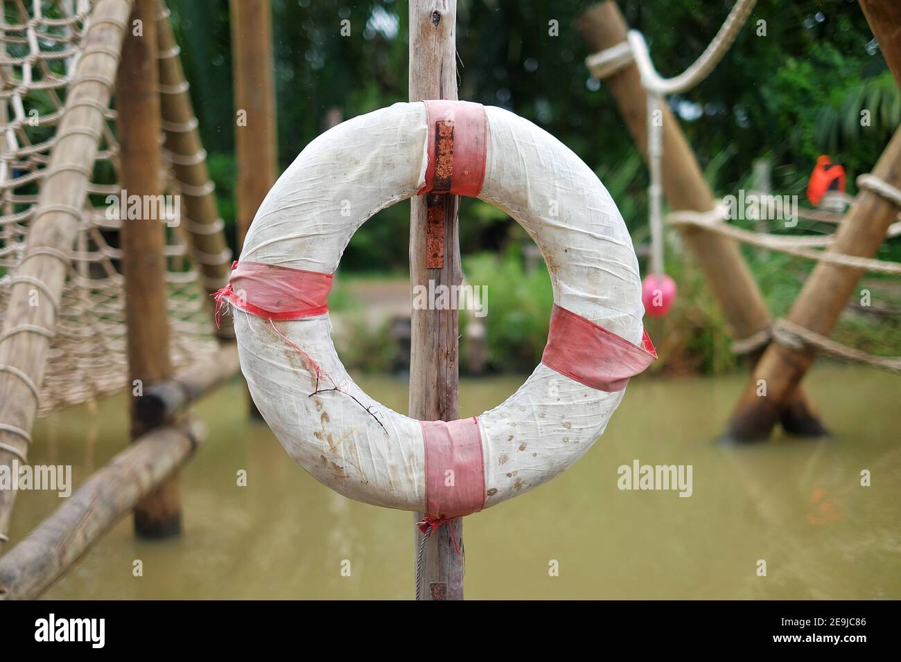 A white and red lifeguard floater hanging on a stick by a river bank. Stock Photo