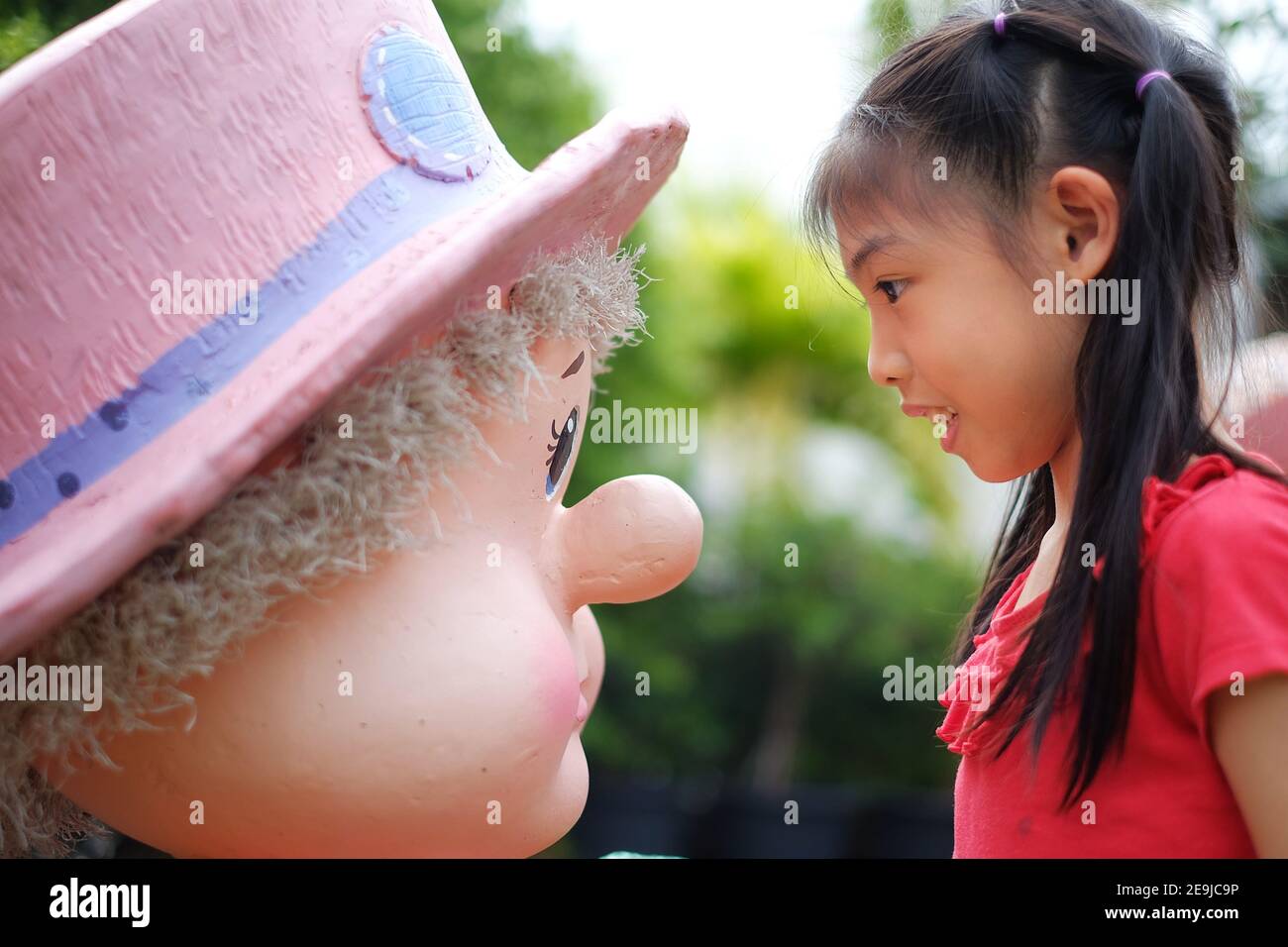 A side view of cute young Asian girl having a face to face staring at a statue, playing and having fun. Stock Photo