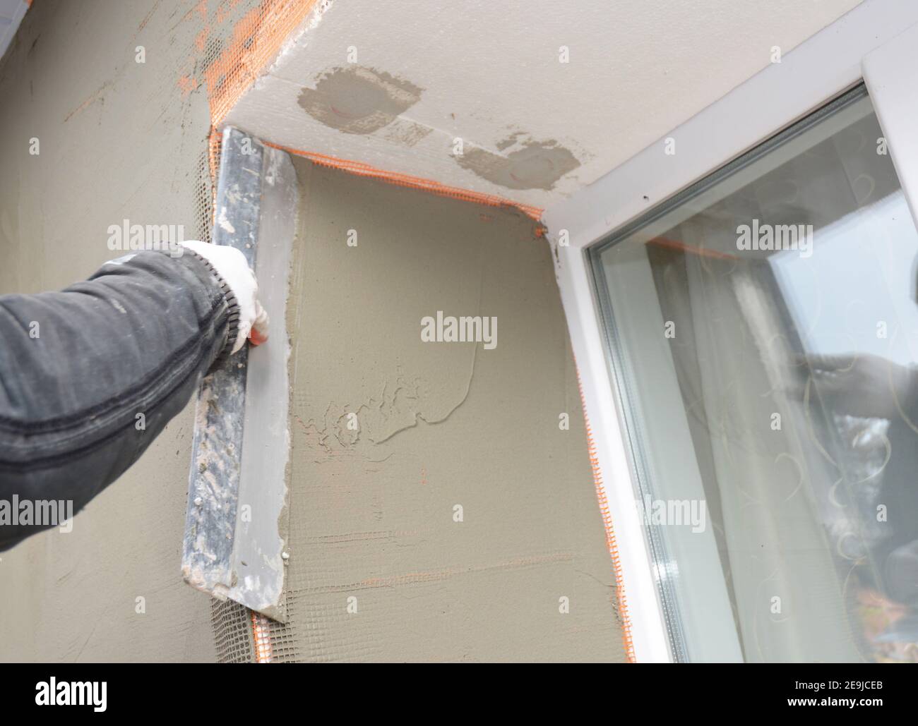 Builder plastering wall with spatula, fiberglass mesh, plaster mesh after foam rigid insulation. Window sill area insulation with stucco wall. Stock Photo
