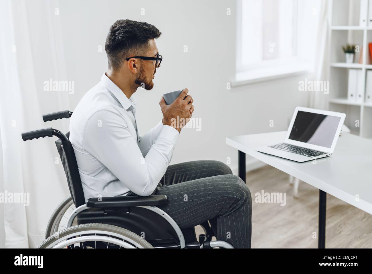 Disabled young businessman drinking coffee at his working table Stock Photo