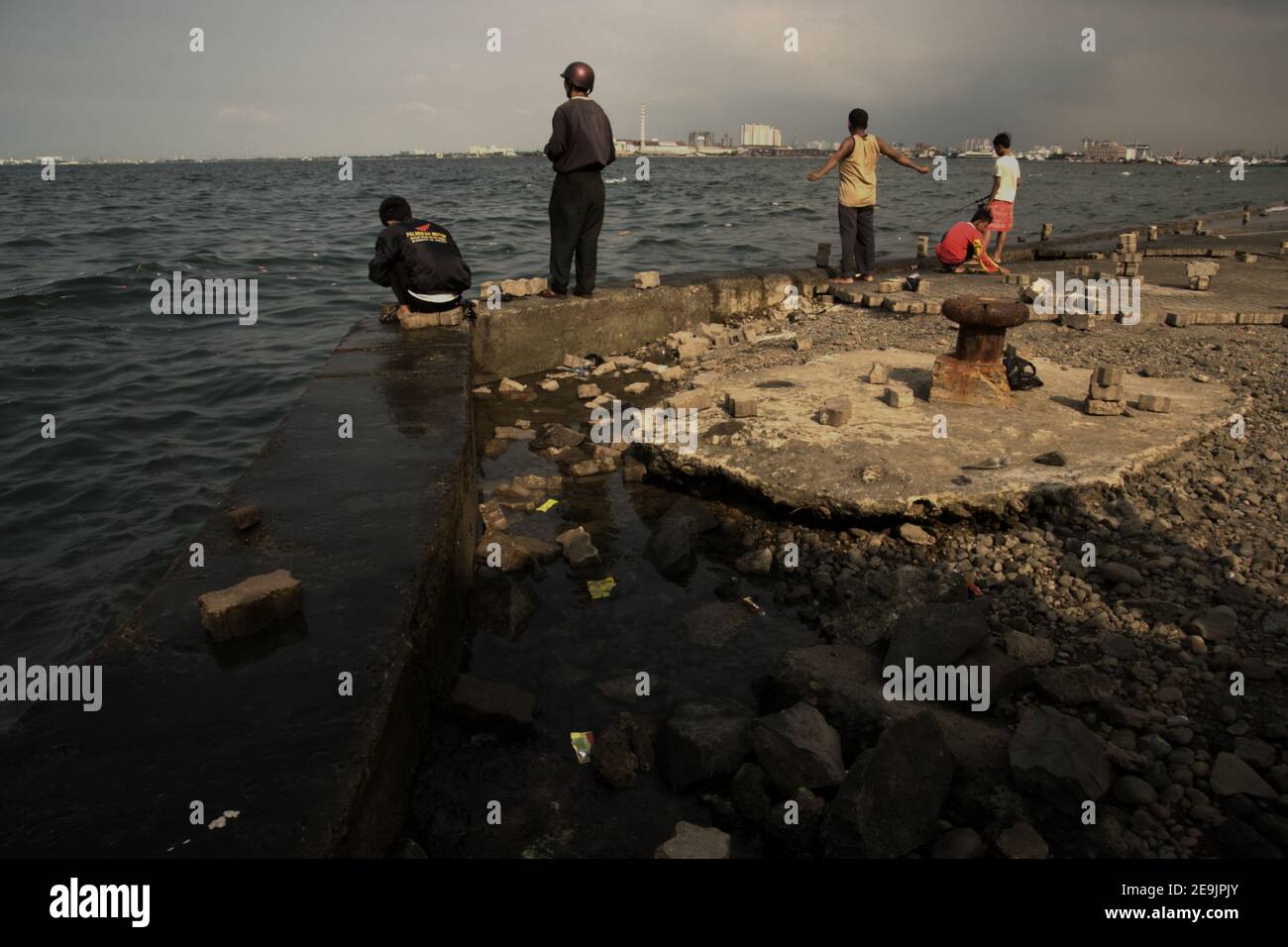 People having outdoor recreation by fishing from an abandoned harbour platform in Muara Baru area, Penjaringan, Jakarta, Indonesia. Stock Photo