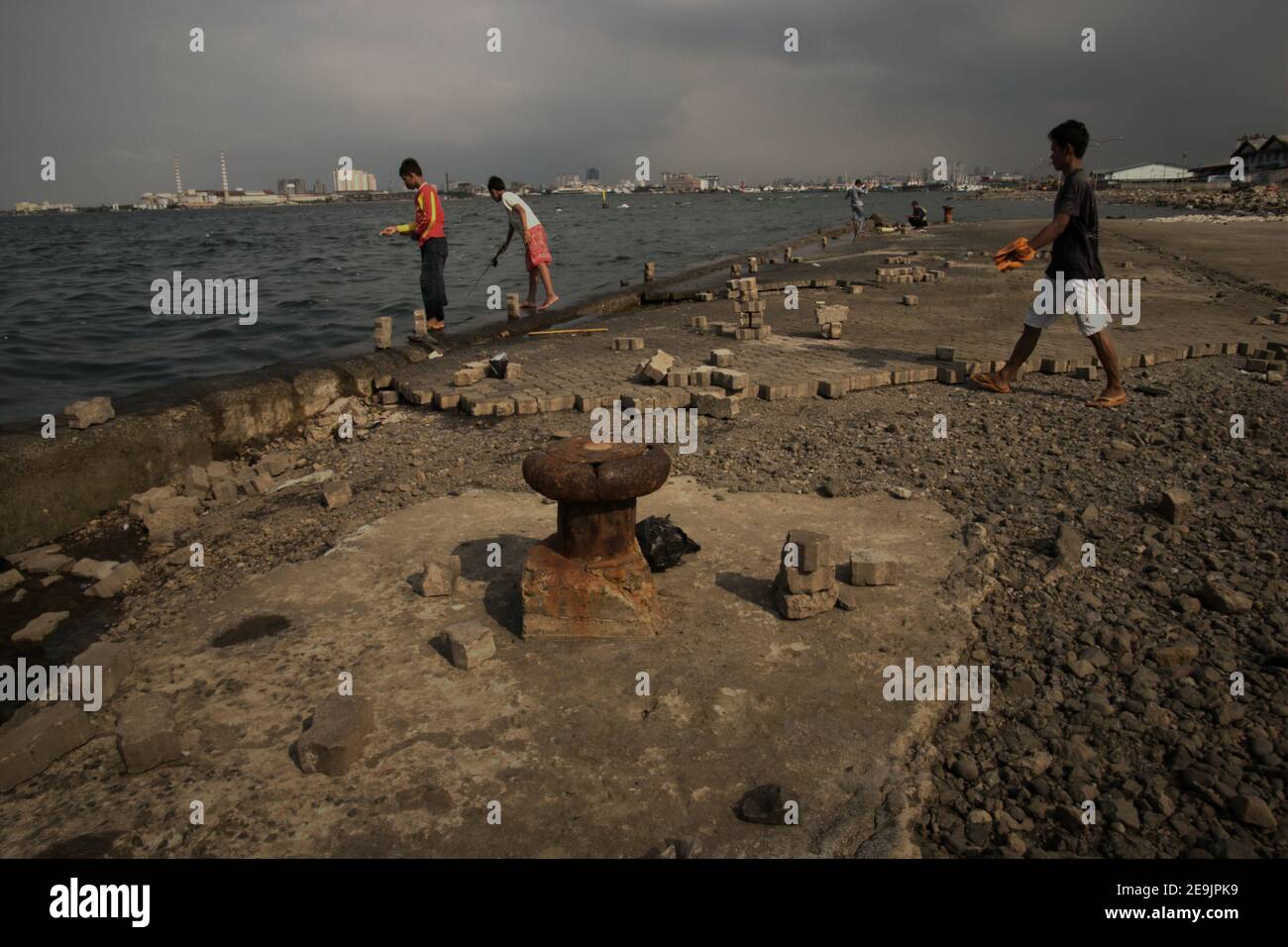 People having outdoor recreation by fishing from an abandoned harbour platform in Muara Baru area, Penjaringan, Jakarta, Indonesia. Stock Photo