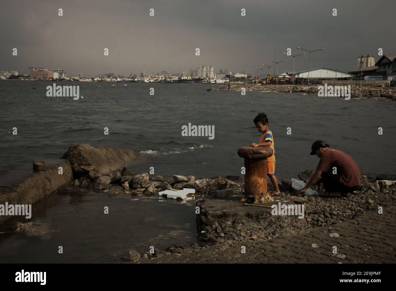 Weather and sea tides have left a harbour platform damage then abandoned, in the coastal area of Jakarta, where a man and child getting ready to have an outdoor recreation by fishing. Muara Baru area, Penjaringan, Jakarta, Indonesia. Stock Photo