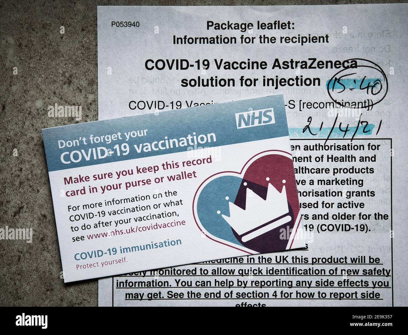 A UK NHS COVID-19 vaccination record card, used to log details of vaccinations given. In the background is the AZ package leaflet. Stock Photo