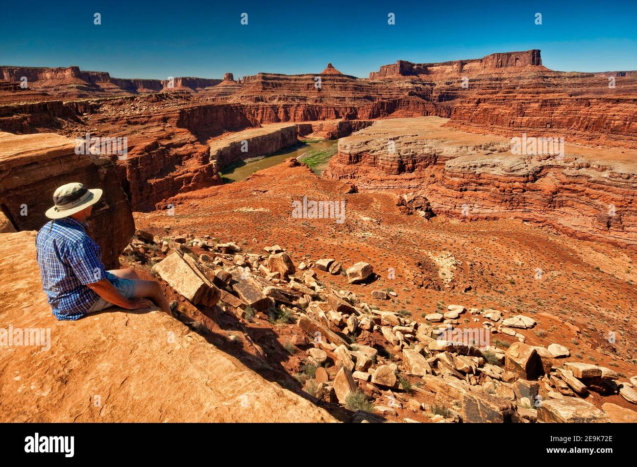 Man sitting at Colorado River Overlook in Walking Rocks area, Dead Horse Point cliffs in distance, White Rim Road, Canyonlands National Park, Utah USA Stock Photo