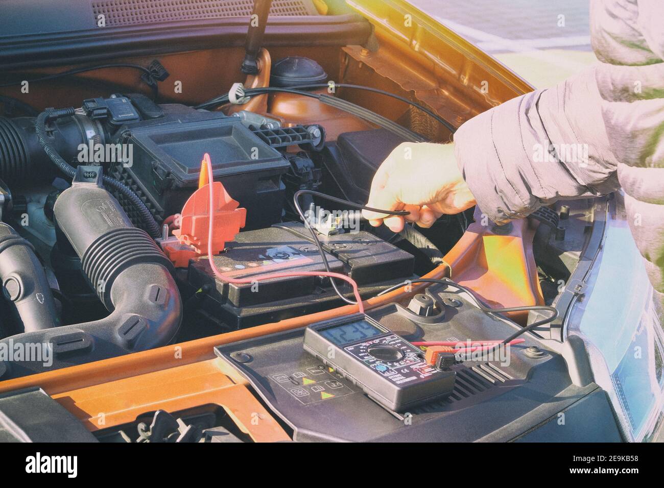Measurement of battery voltage in a car. Driver inspection holding battery capacity tester voltmeter. Toned image. Stock Photo