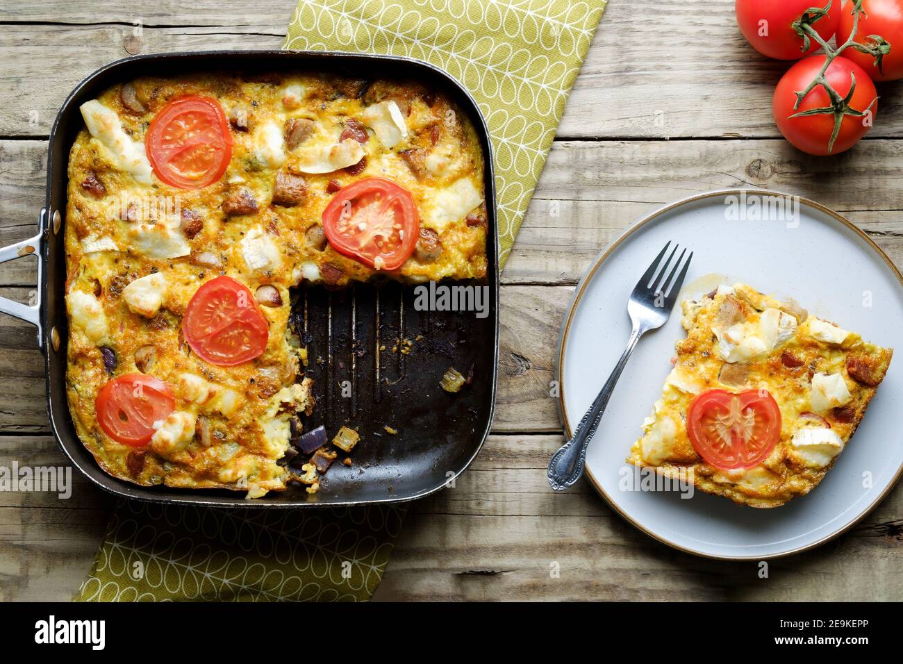A freshly made Goat Cheese Frittata. The full Frittata is shown in the cooking pan with a slice onesie plate. An egg based healthy eating option Stock Photo