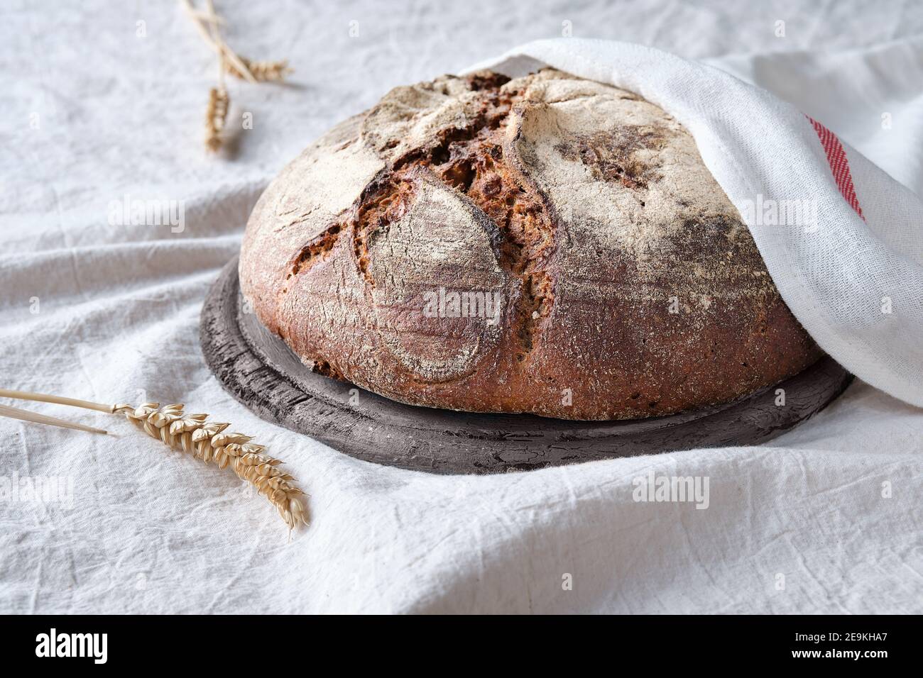 No knead handmade loaf on cutting board on textile with linen towel, spelt ears. German Bauernbrot means Farmers Bread in English. Wholemeal rye wheat Stock Photo