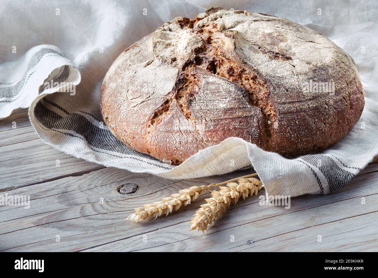 No knead handmade loaf on cutting board on wood with linen towel, spelt ears. German Bauernbrot means Rustic Farmers Bread in English. Wholemeal rye Stock Photo