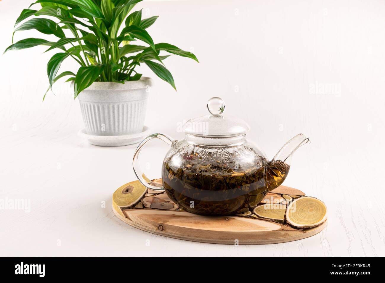 glass teapot with herbal tea on a wooden juniper stand and a green plant on  a white wooden table Stock Photo - Alamy